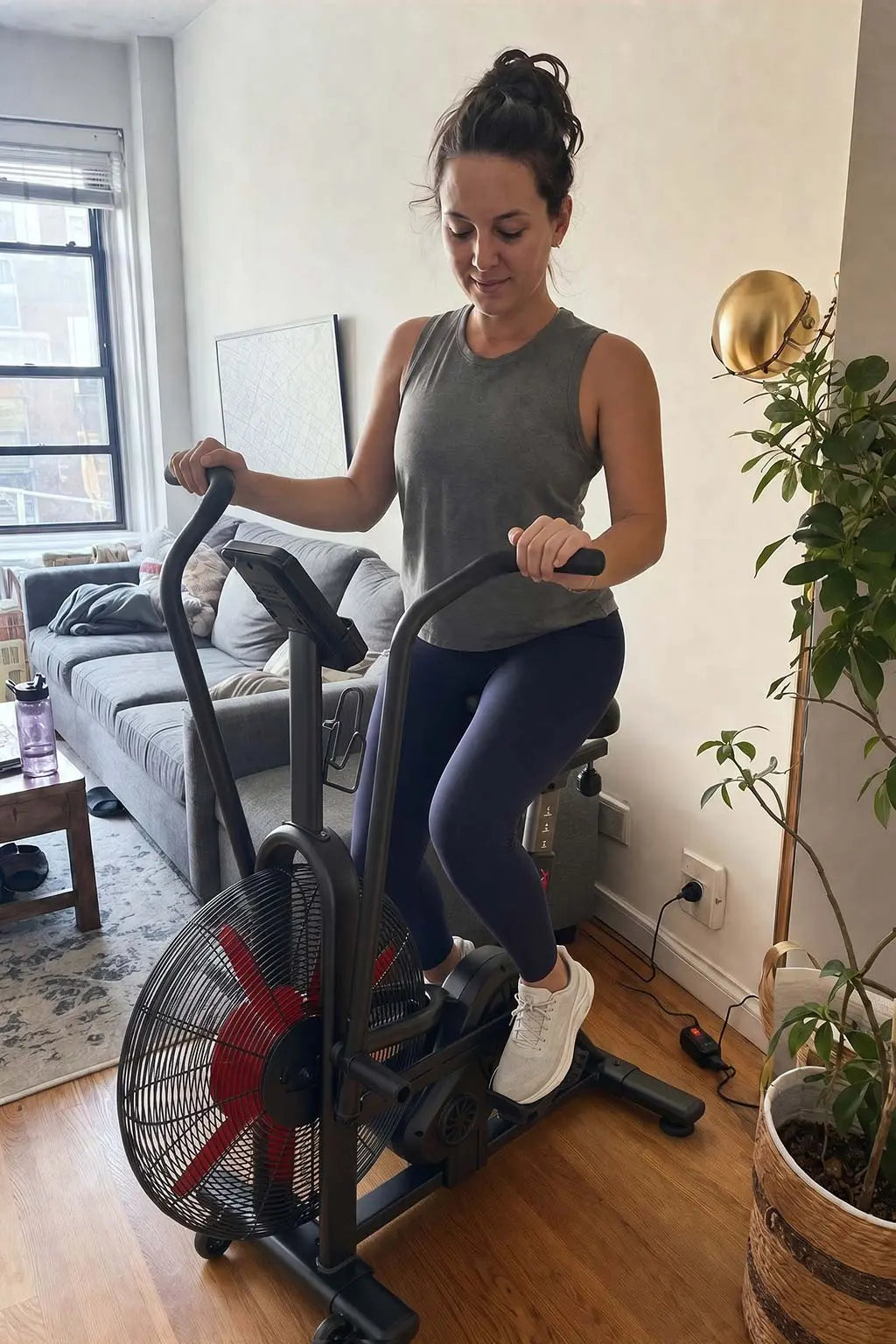 A woman working out on a Wenoker air resistance exercise bike with moving handlebars in an apartment living room.